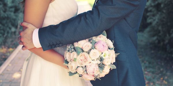 Bride and groom embracing with a bouquet of flowers between them.