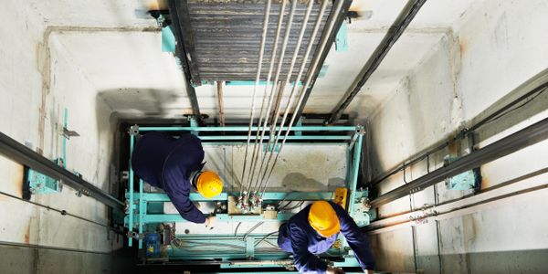 Two workers wearing helmets working inside an elevator shaft.