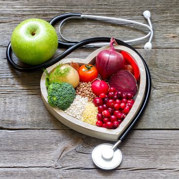 A heart-shaped platter with various fruits and vegetables beside a stethoscope
