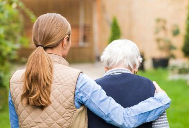 A woman comforting an elderly person outdoors.