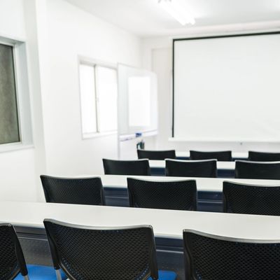 Empty classroom with black chairs and a projector screen.