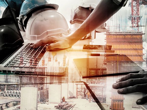 Engineer working on laptop with construction site overlay and safety helmets.