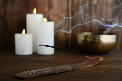 Burning incense stick with candles in the background.