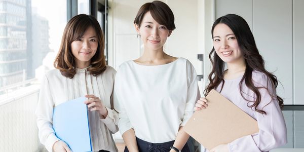 Three professional women smiling and holding folders in an office.