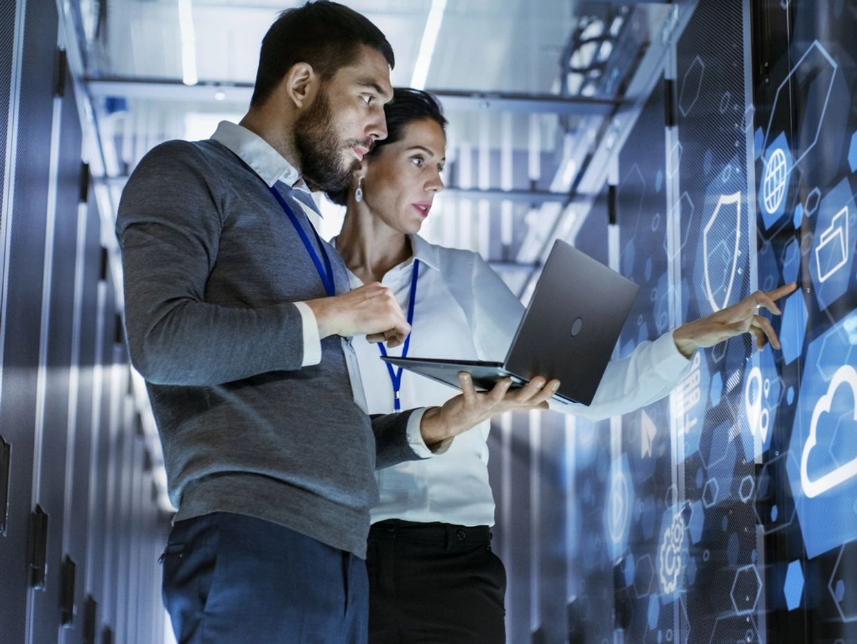 Two professionals analyzing digital data on a transparent screen in a server room.