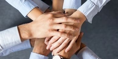 Multiple hands stacked in teamwork gesture.