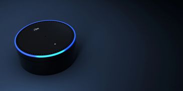 Black smart speaker with blue light ring on dark surface.