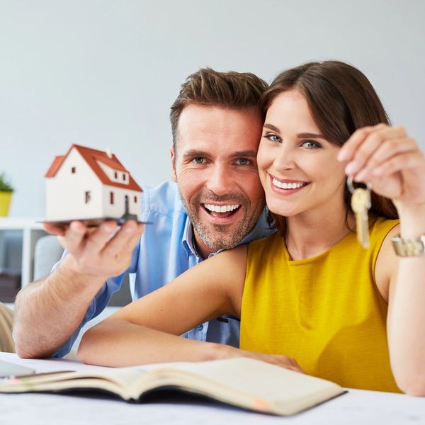 Happy couple holding house model and keys, celebrating home ownership.