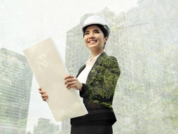 Smiling female architect in a hard hat holding blueprints with city and nature overlay.