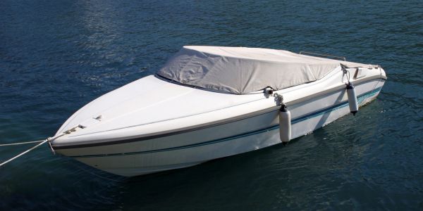 A white boat covered with a gray tarp floating on water.