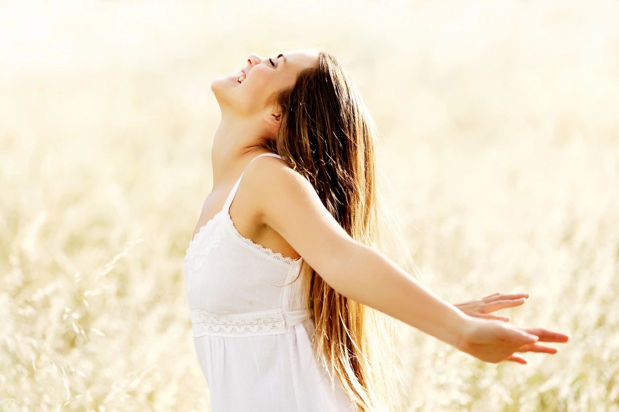 Lady in a white dress, in a corn field with her arms flung behind her looking very happy and free. 