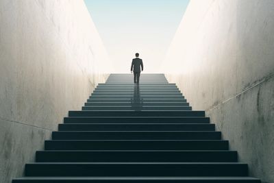 A person walking up a long, dark staircase towards a bright opening.
