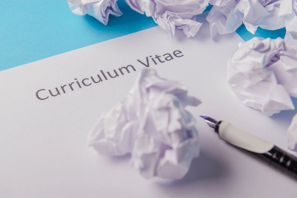 Crumpled papers around a curriculum vitae sheet and a pen.