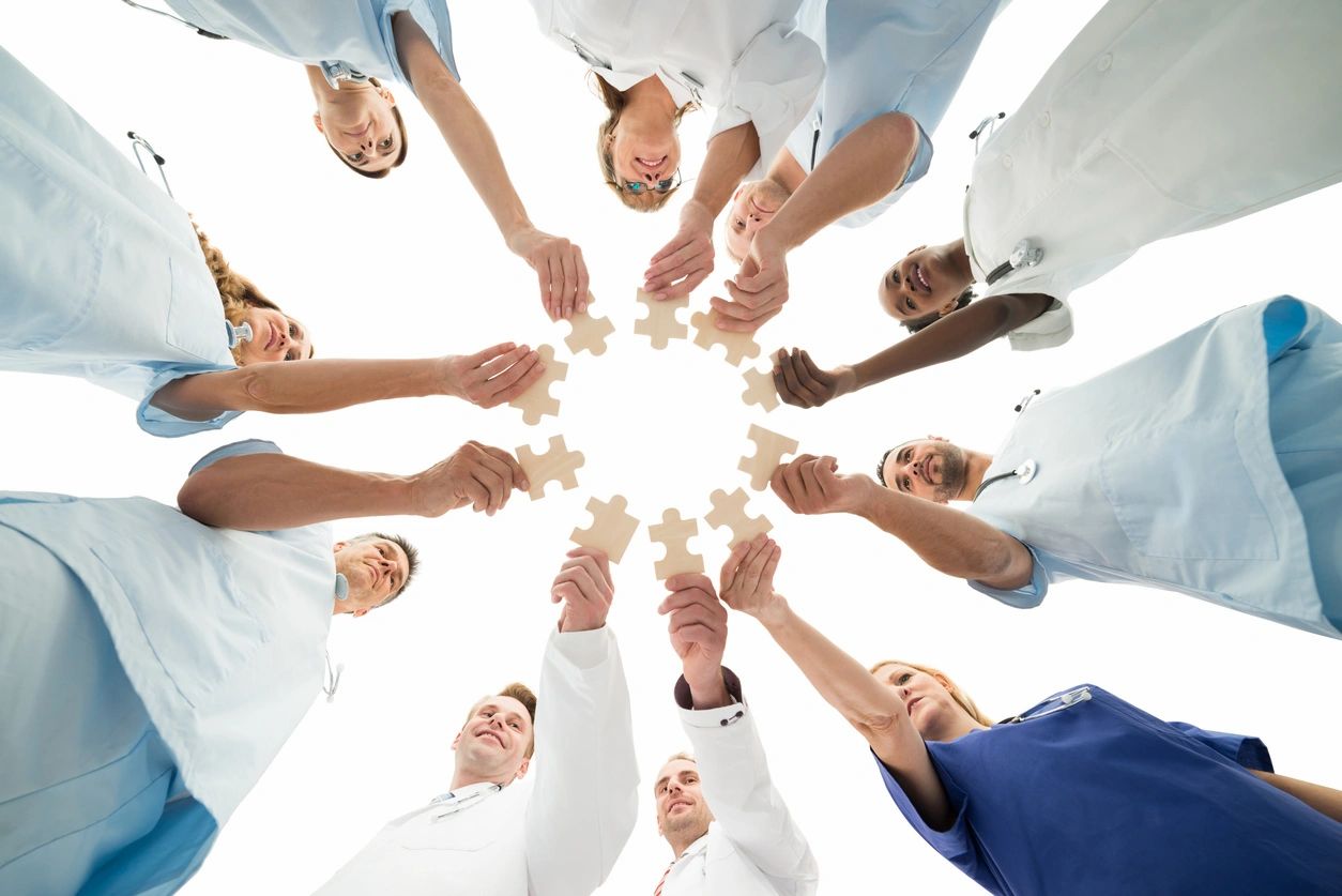 Photo from below of people in a circle one arm outstretched holding jigsaw pieces. 