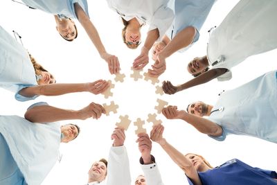 Team of diverse professionals holding puzzle pieces in a circle symbolizing collaboration.