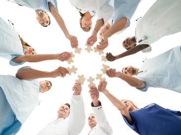 Medical professionals holding puzzle pieces in a circle symbolizing teamwork.