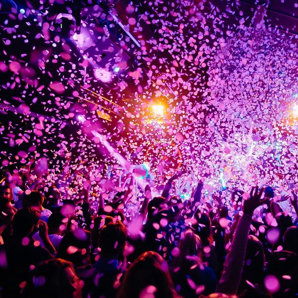 Crowd celebrates under a shower of pink confetti at a vibrant party.