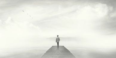 A lone figure walks on a pier into a foggy, endless horizon.