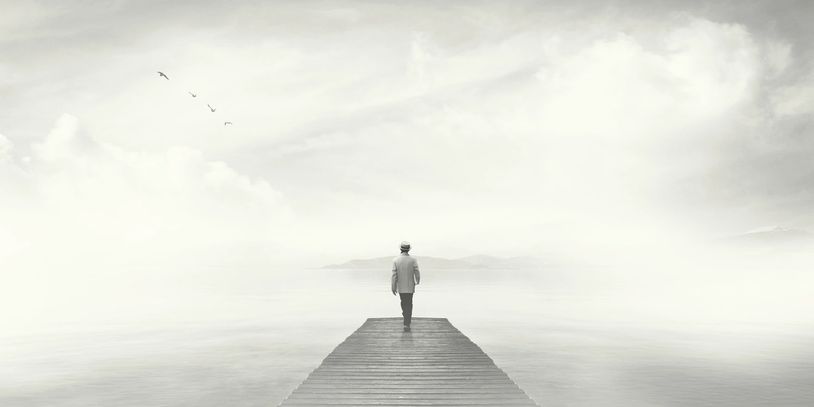 A solitary figure walks on a pier into a foggy, serene landscape.