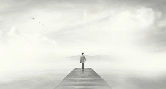 a person standing at the end of a dock, looking out over a lake, shrouded in fog