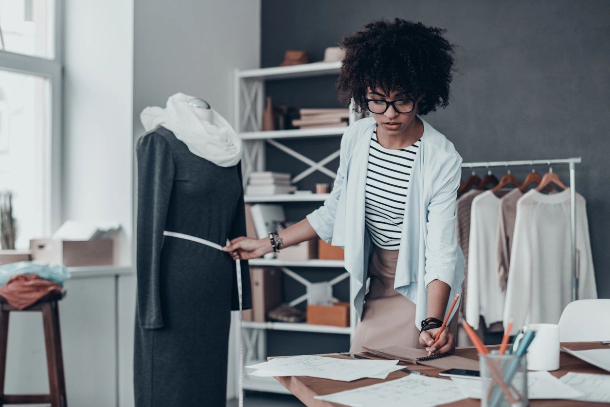 A fashion designer measuring a dress on a mannequin and sketching designs.