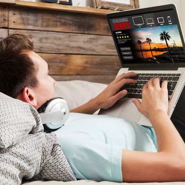 Person lying on a couch browsing streaming series on a laptop.