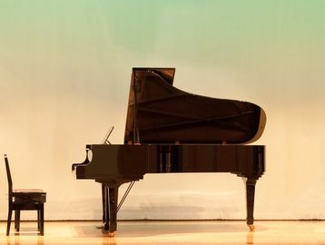 A grand piano and a chair on a stage with a plain backdrop.