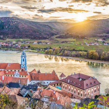 Sunset over a charming riverside village with red-roofed buildings and hills.