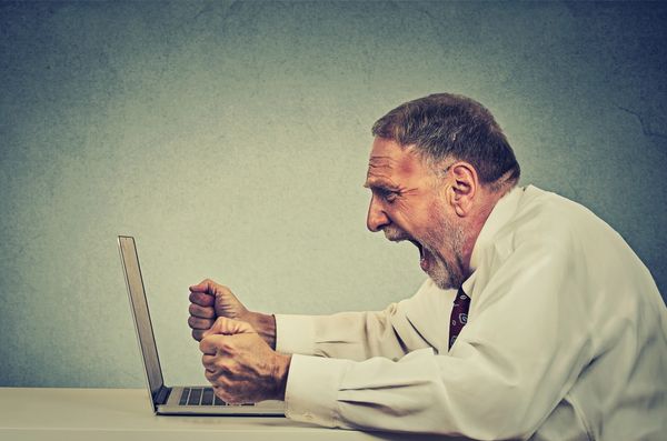 An angry old man sitting in front of a laptop 