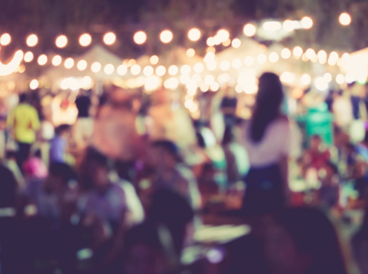 Blurred crowd at an outdoor nighttime event with string lights.