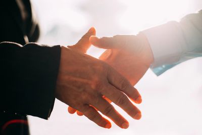 A close-up image of two individuals about to shake hands on a sunny day.