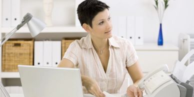 Woman working in an office with a laptop and fax machine.