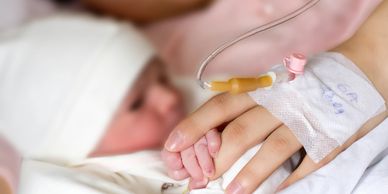 Newborn baby holding mother's hand with IV drip visible.