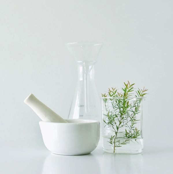 A mortar and pestle sitting next to chemistry beakers featuring natural botanicals.