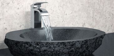 Modern faucet pouring water into a textured black stone sink.