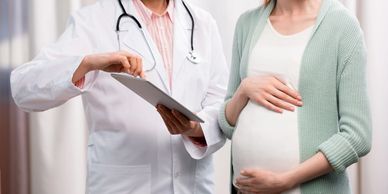 Pregnant woman consulting a doctor holding a clipboard.