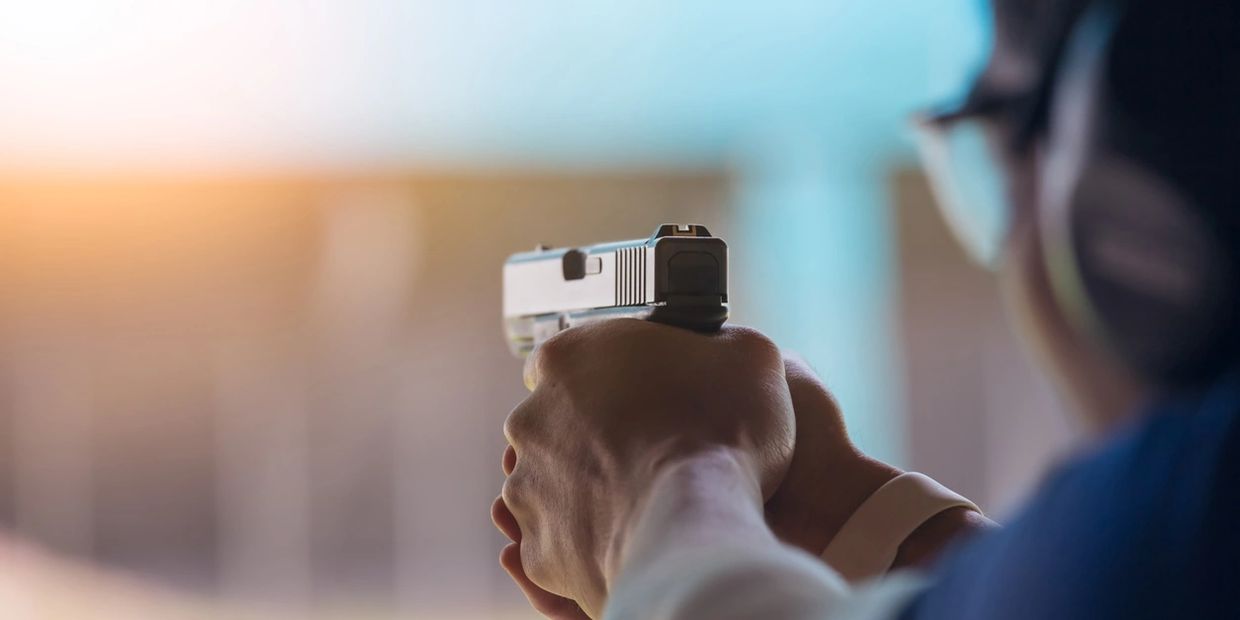 Person aiming a handgun at a shooting range, wearing safety gear.