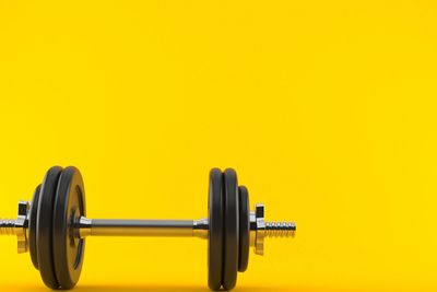 Black dumbbell on a bright yellow background.