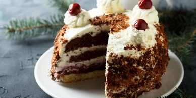 Chocolate cake with cherries and whipped cream on top, sliced to show layers.