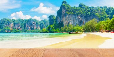 Tropical beach in Thailand with longtail boats and limestone cliffs.