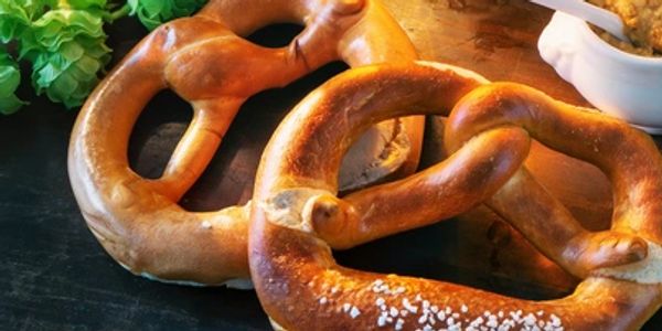Two golden-brown pretzels on a dark surface with fresh greens.