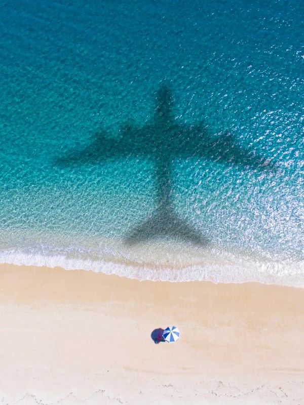 Airplane shadow over beach water near umbrella.