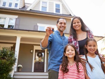 Man, woman, and two children stand in front of a house, smiling. Man is holding a key.