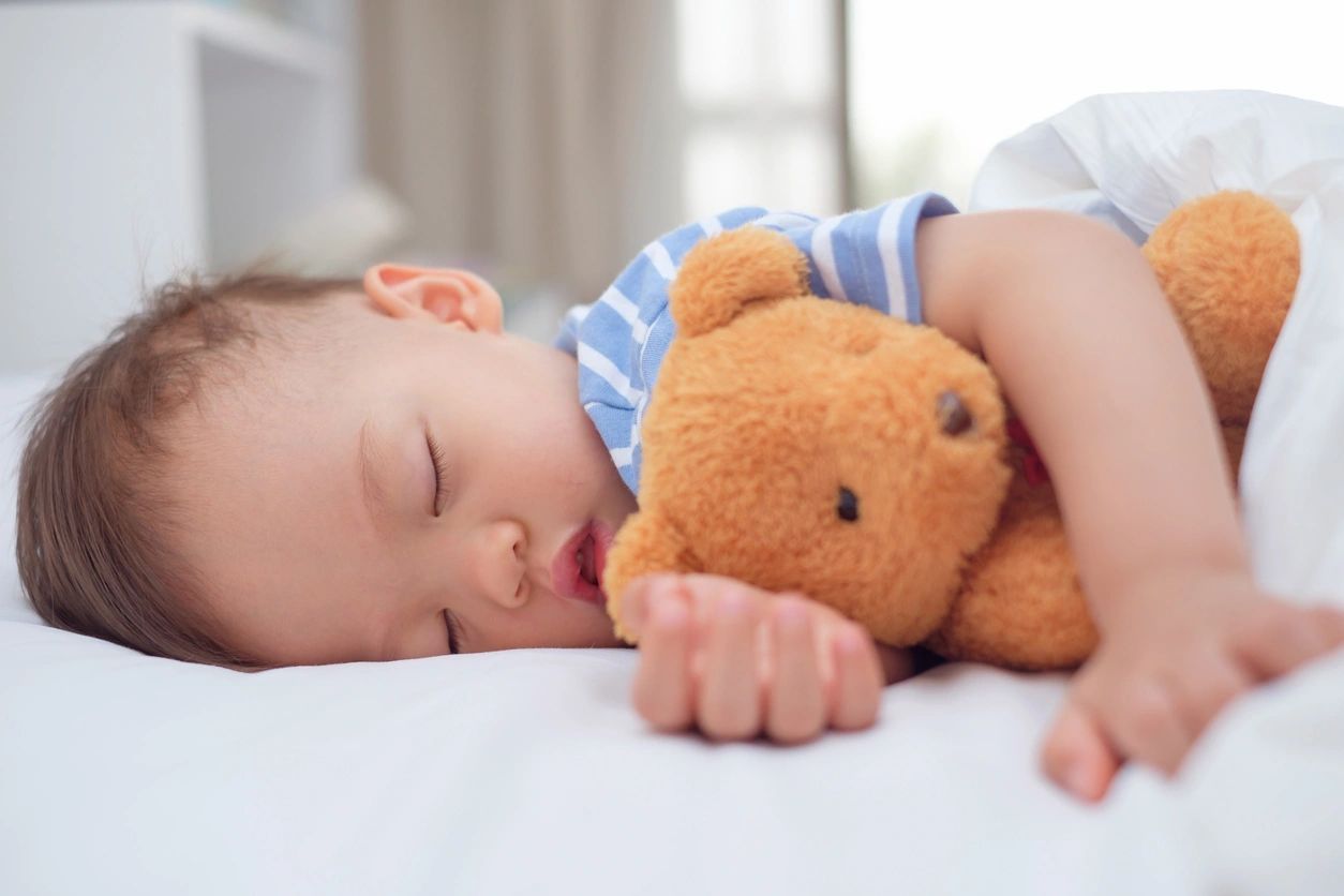 Baby peacefully sleeping while hugging a teddy bear.