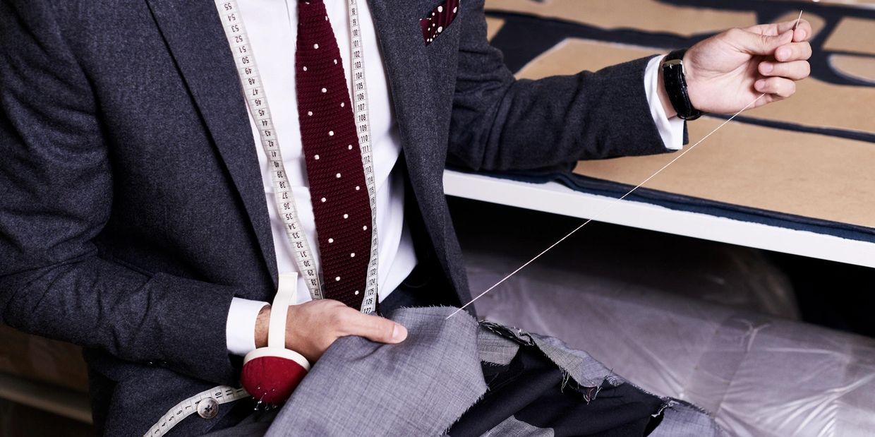 A tailor sewing a gray suit with a needle and thread.