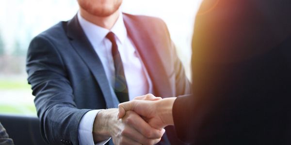Two executives shaking hands with the sun shining behind them
