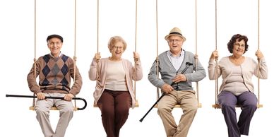 Four elderly people happily sitting on swings, two holding canes.