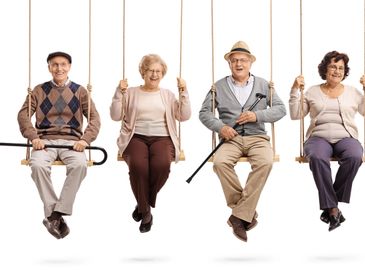 Four elderly friends joyfully sitting on swings with canes.