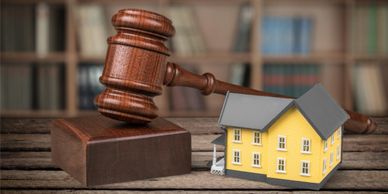 A judge's gavel sits on a wooden platform next to a miniature house. 