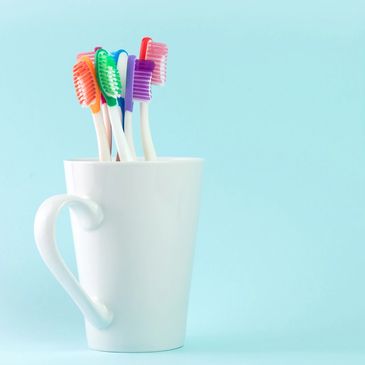 Colorful toothbrushes in a white mug against a blue background.